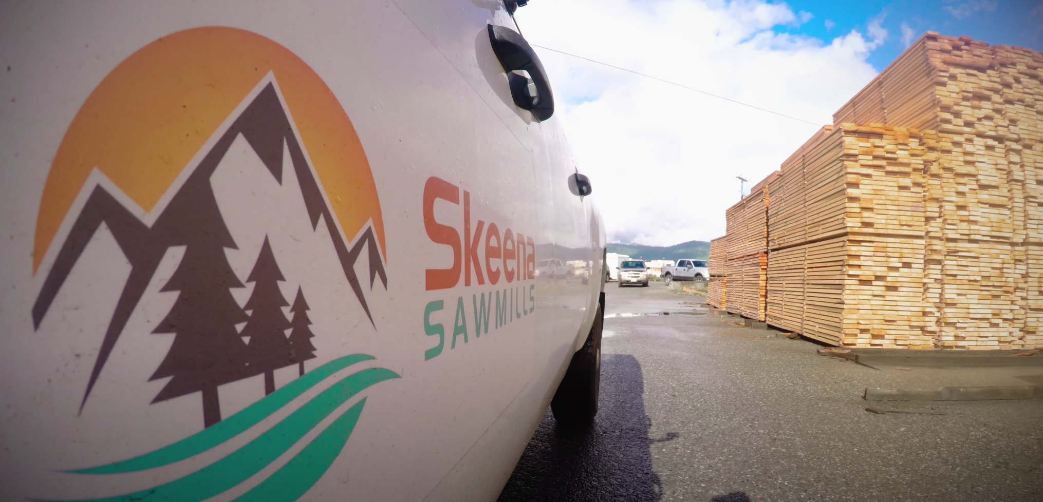 A white pickup truck with the Skeena Sawmills logo on the side drives through the mill's lumber yard.