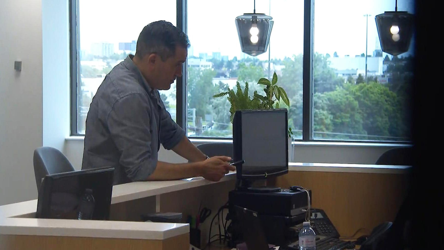 A man in a light blue shirt leans on an office desk.