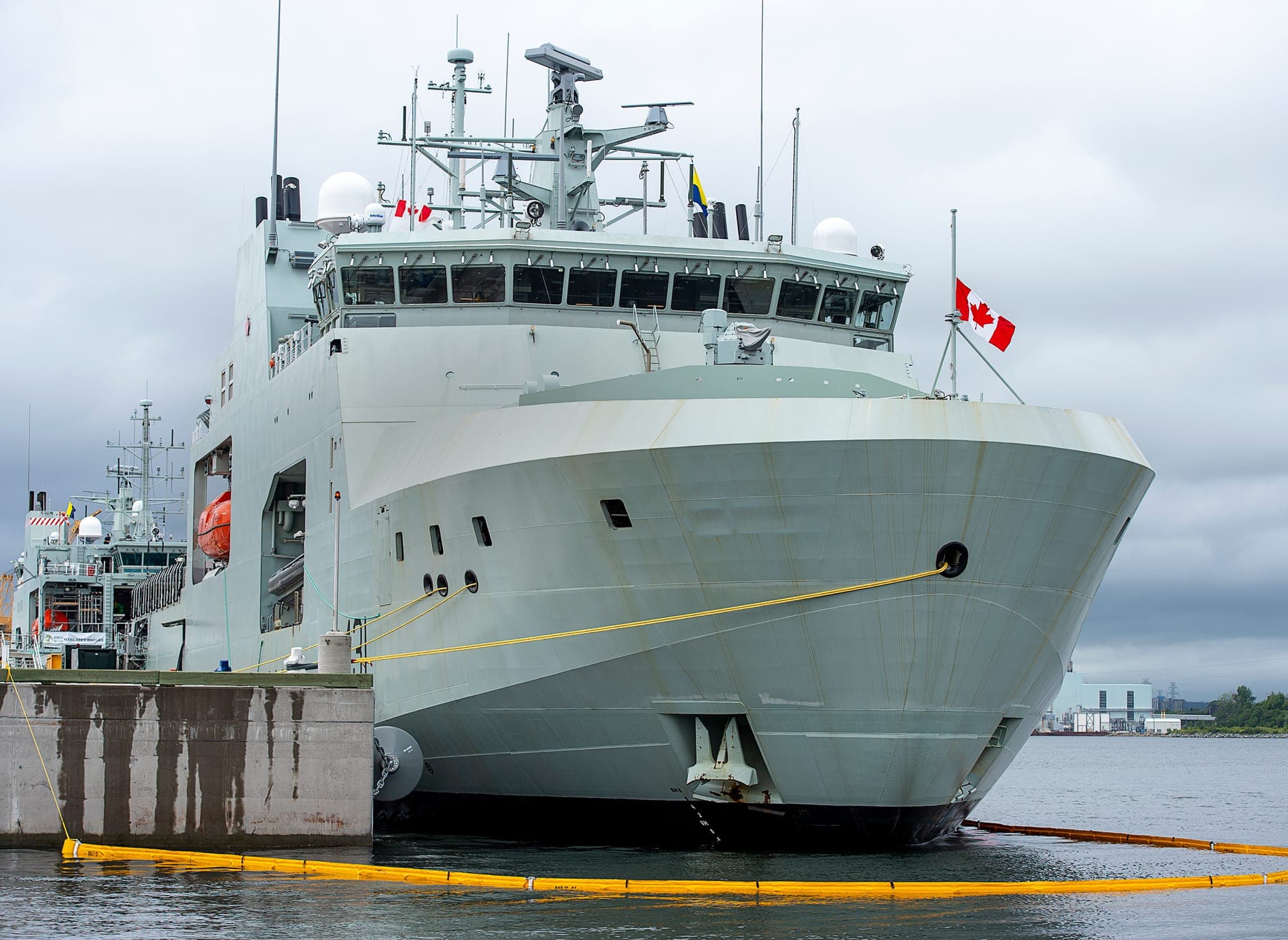 A large white ship with Canadian flags atop is is docked at harbour.