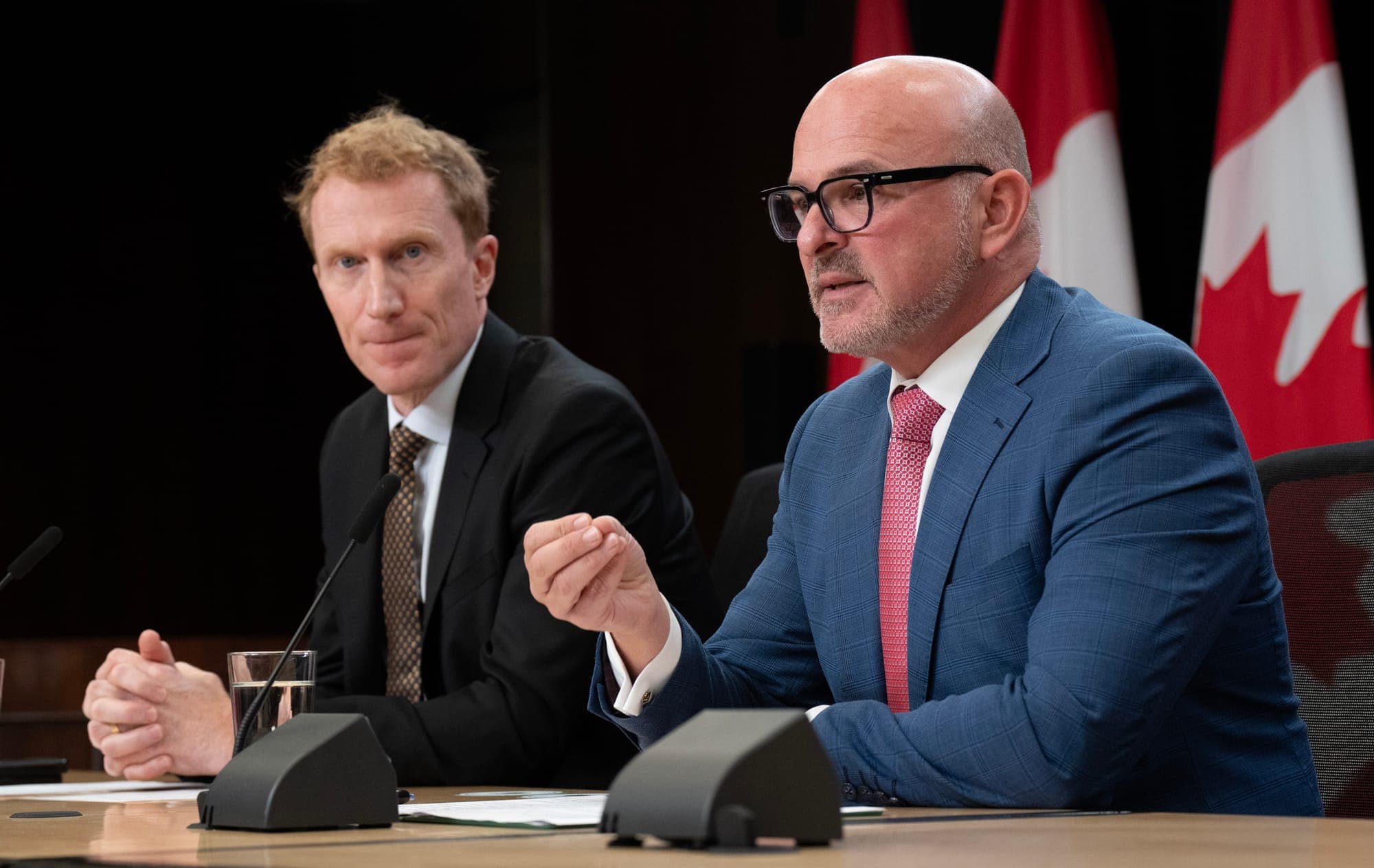 Immigration minister Marc Miller and employment minister Randy Boissonnault are seated at a table at a news conference