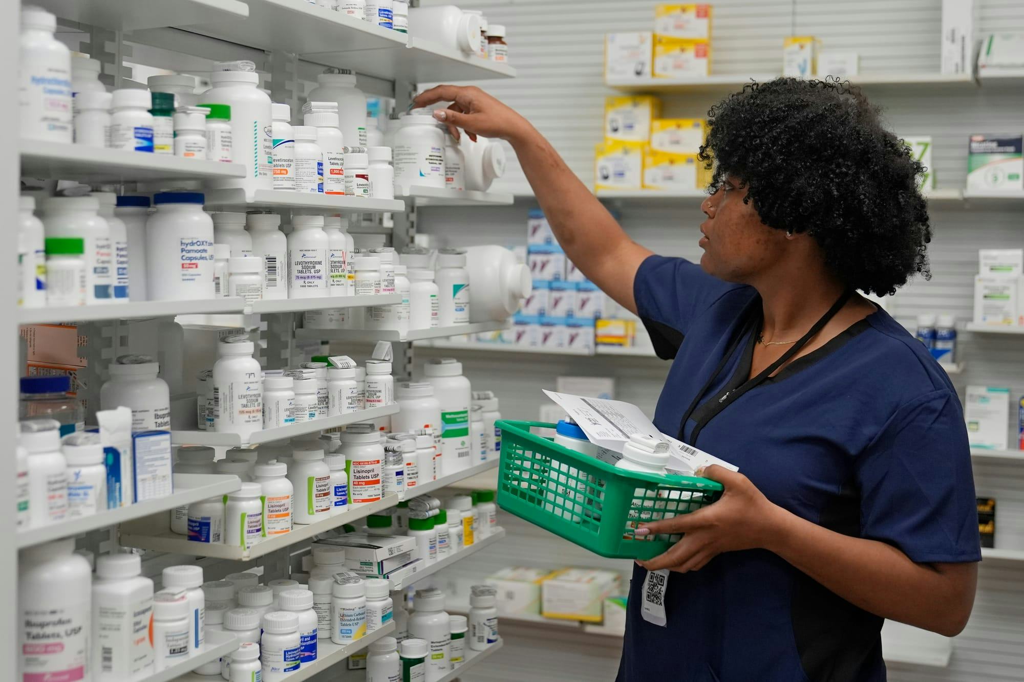 An employee places drugs on a shelf inside a pharmacy.