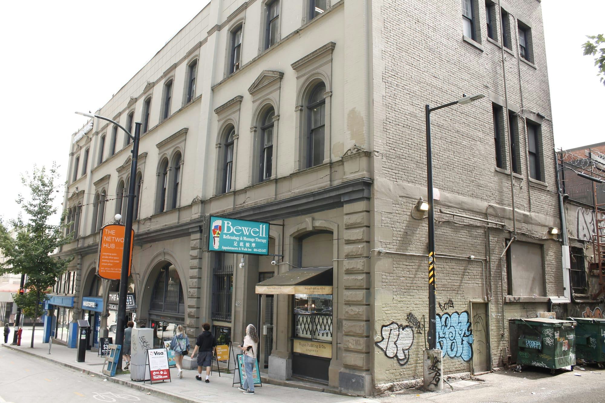 A three-storey grey building in downtown Vancouver with a vegan pudding shop and a massage parlour on its storefront.