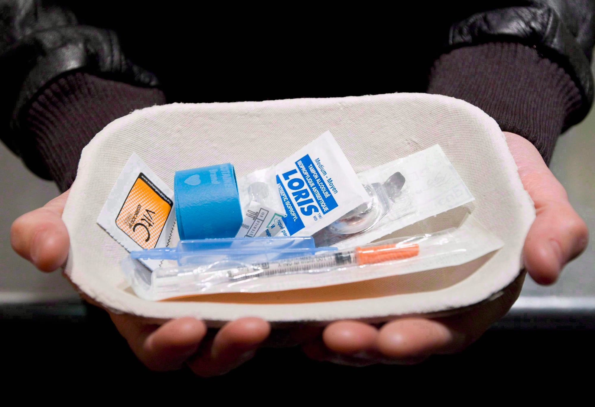 Hands hold a safe injection kit, which includes disinfectant wipes and a syringe.