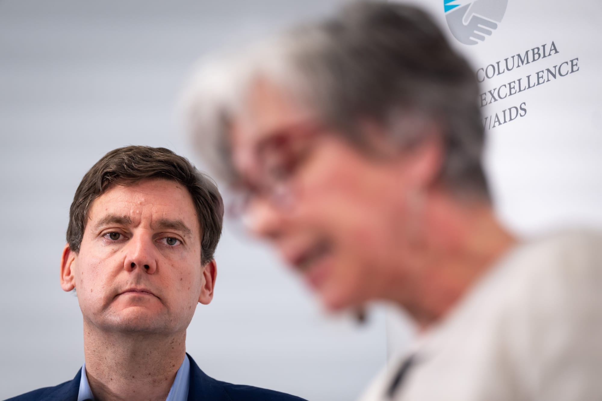 Premier David Eby is shown, in focus, listening as an out-of-focus Minister Jennifer Whiteside makes an announcement.