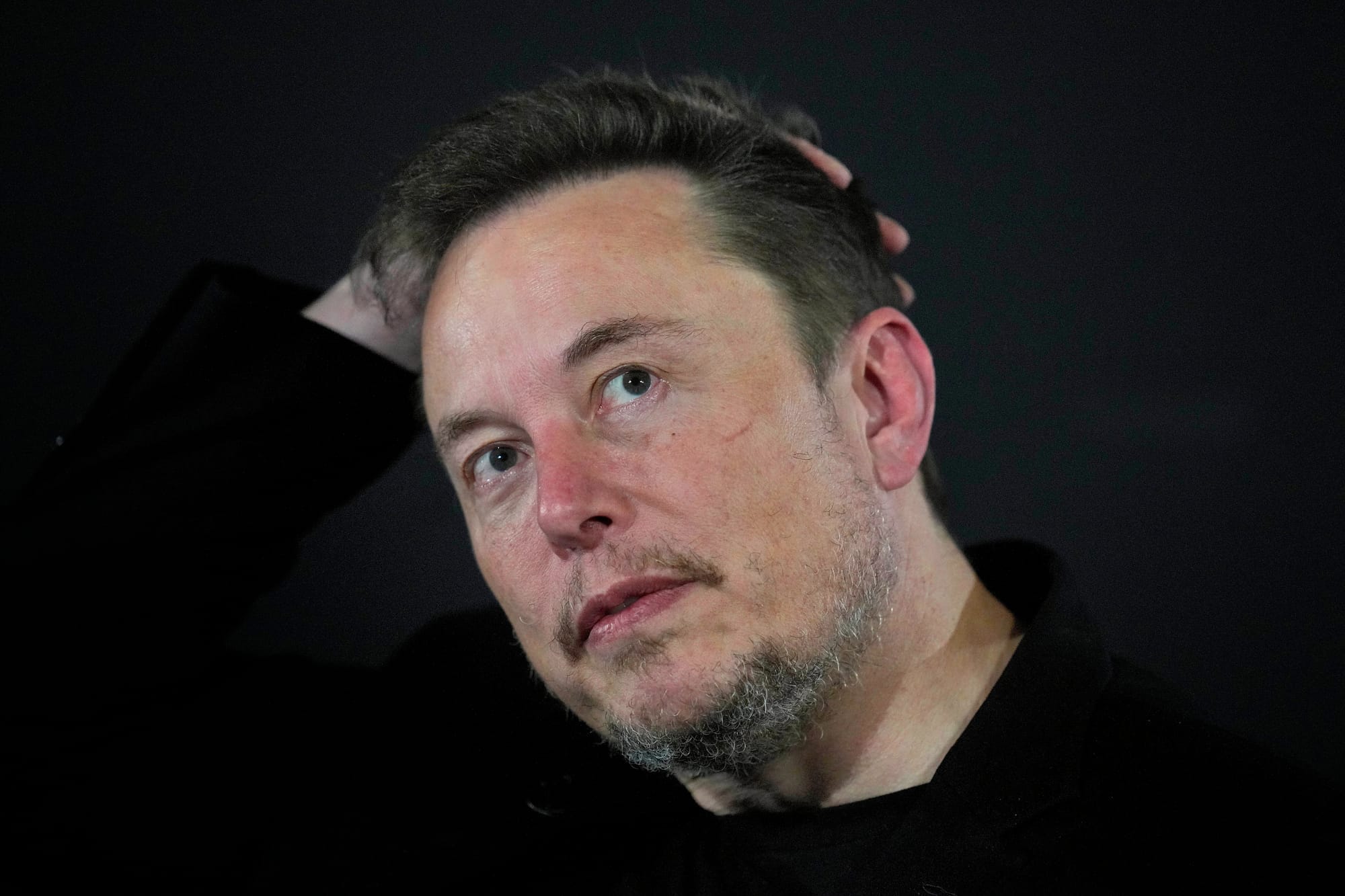 A close up of Elon Musk against a black background.