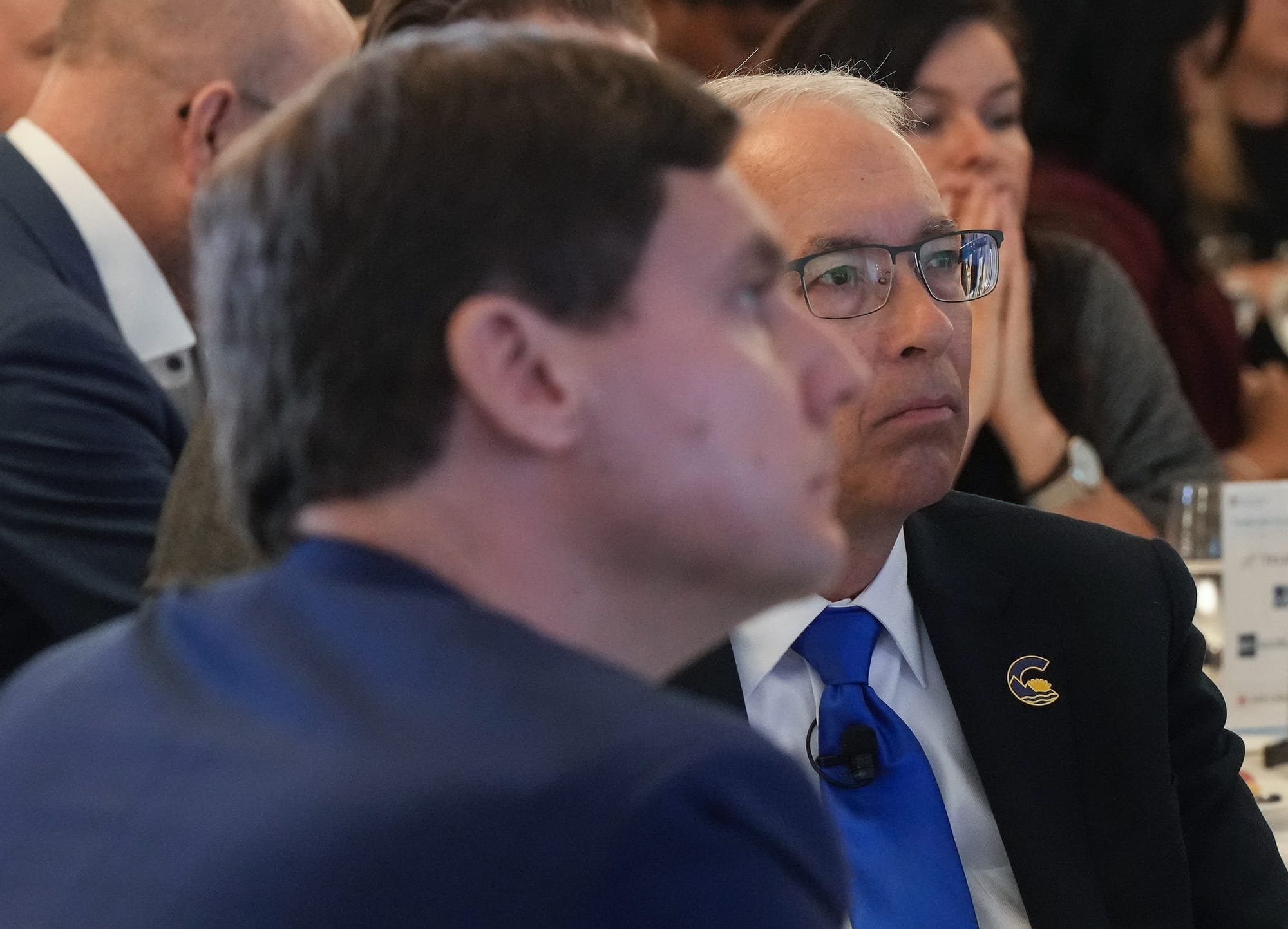 David Eby and John Rustad are shown from the shoulders up, sitting next to each other at an event.