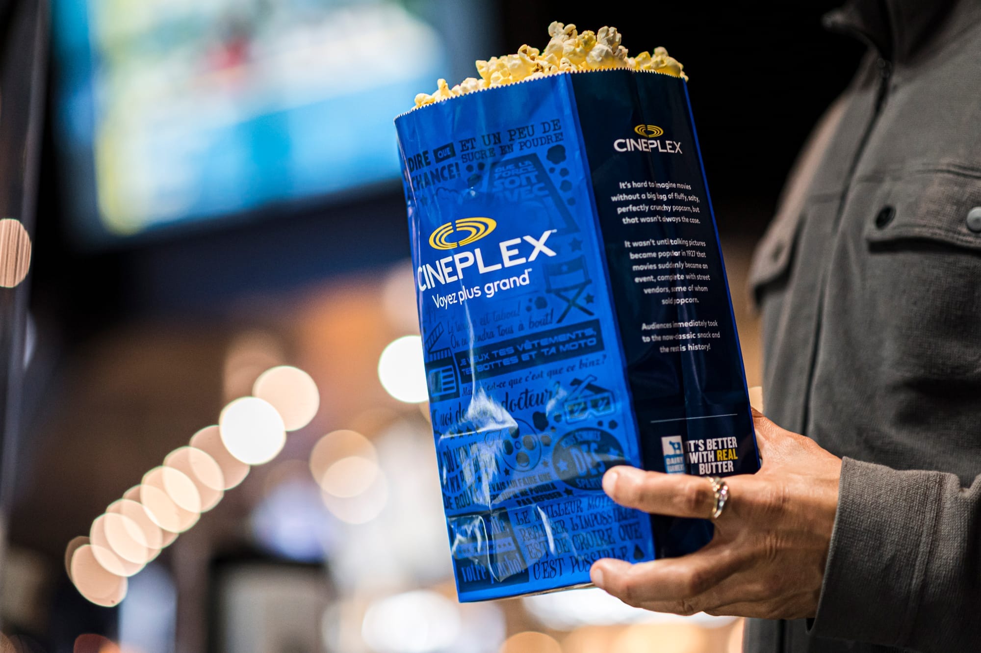 A hand holds a bag of popcorn with a Cineplex logo