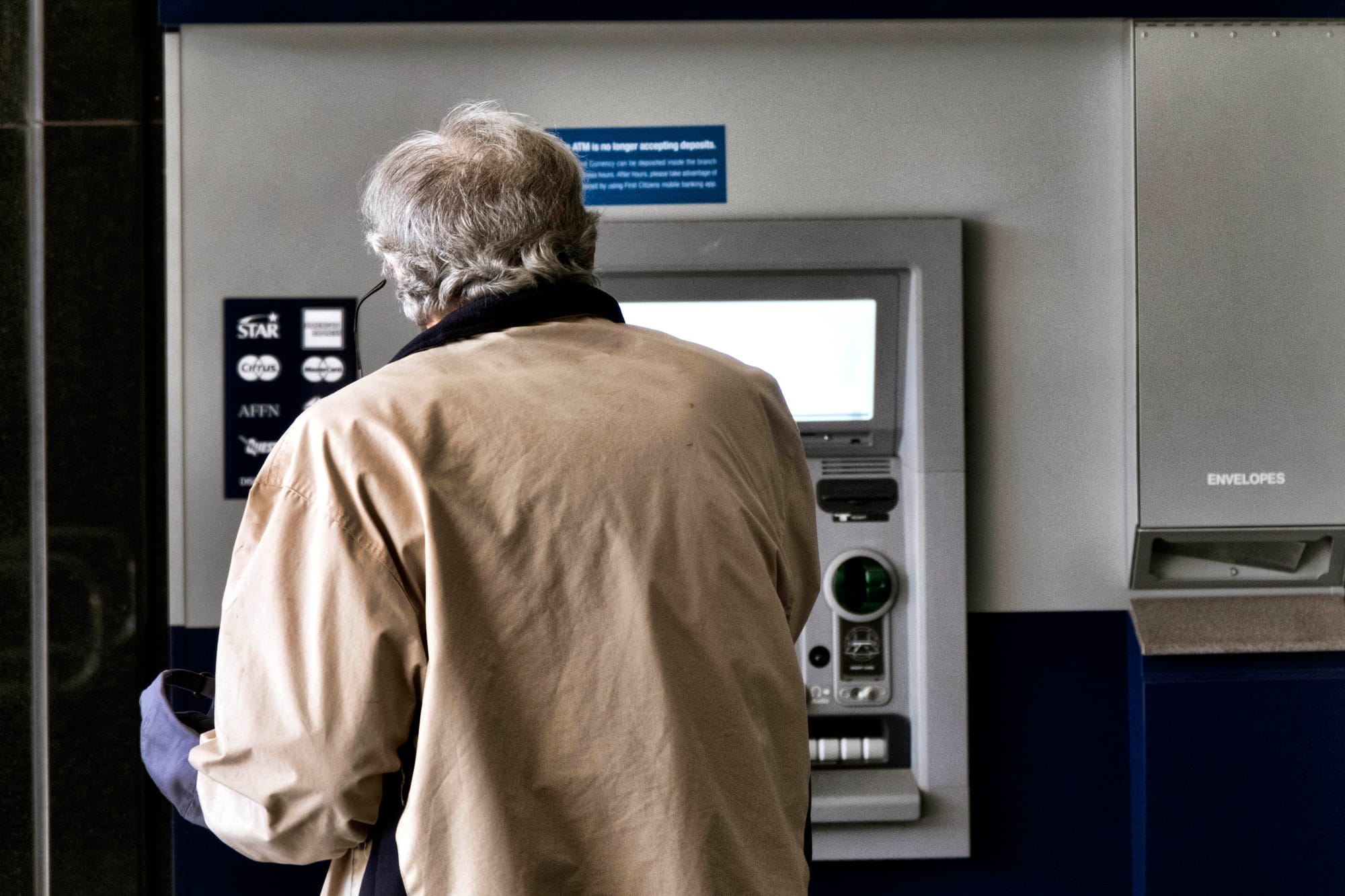 A person with grey hair is shown from behind using an ATMat a Bank.