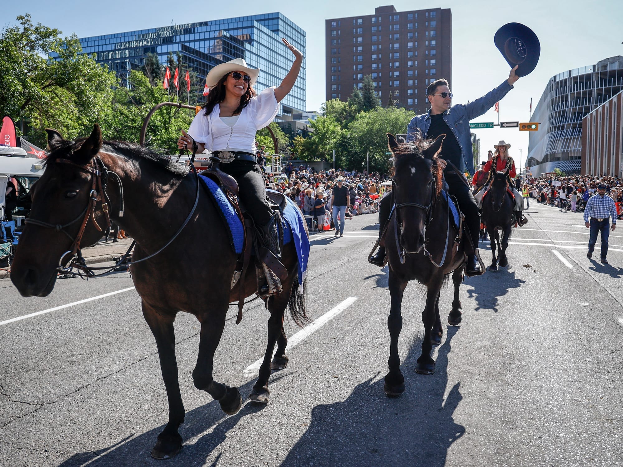 Anaida and Pierre Poilievre sit atop horses and wave to crowds as they ride down a Calgary street.