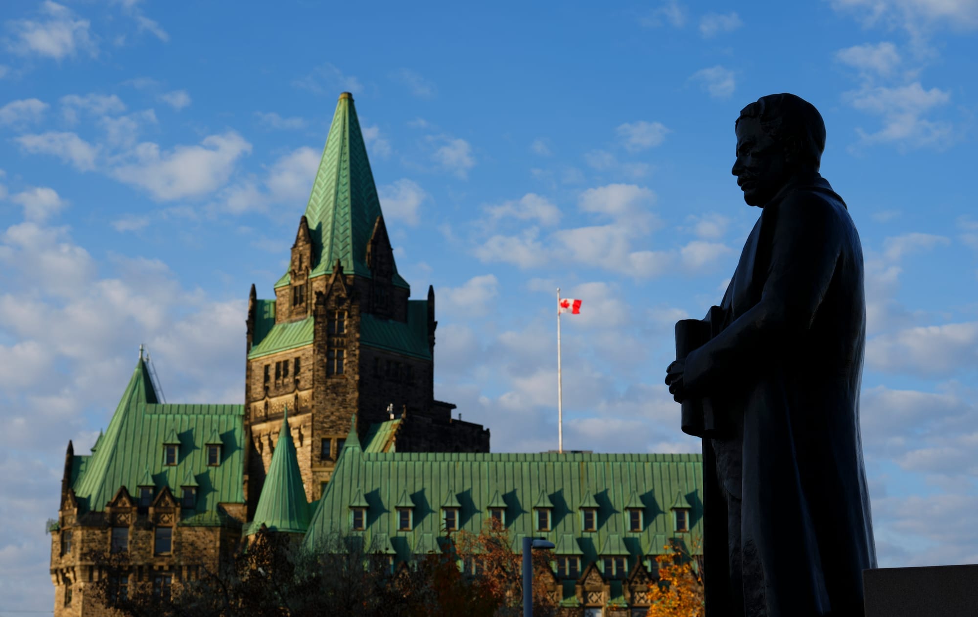 Statue is in the foreground of a the Confederation building against a blue sky  