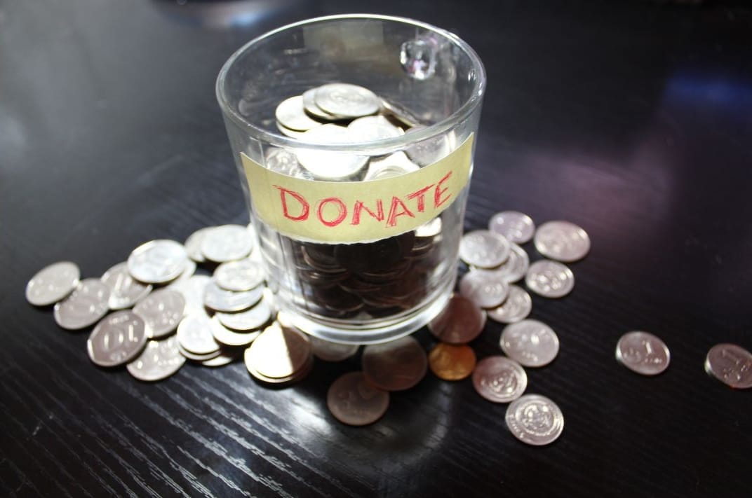 A glass mug with a label reading 'donate' is filled with and surrounded by quarters.