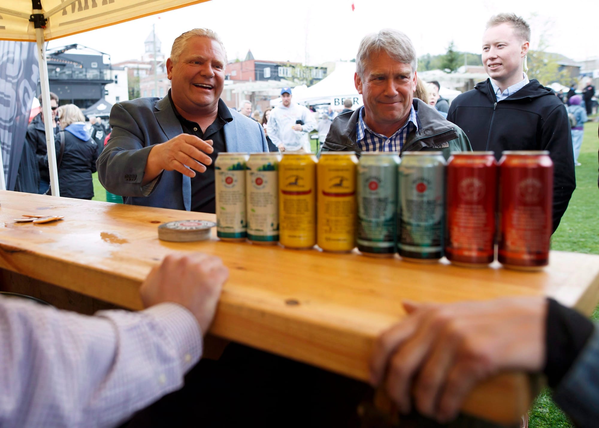 Doug Ford smiles and reaches toward a can of craft beer on display at an outdoor beer festival.