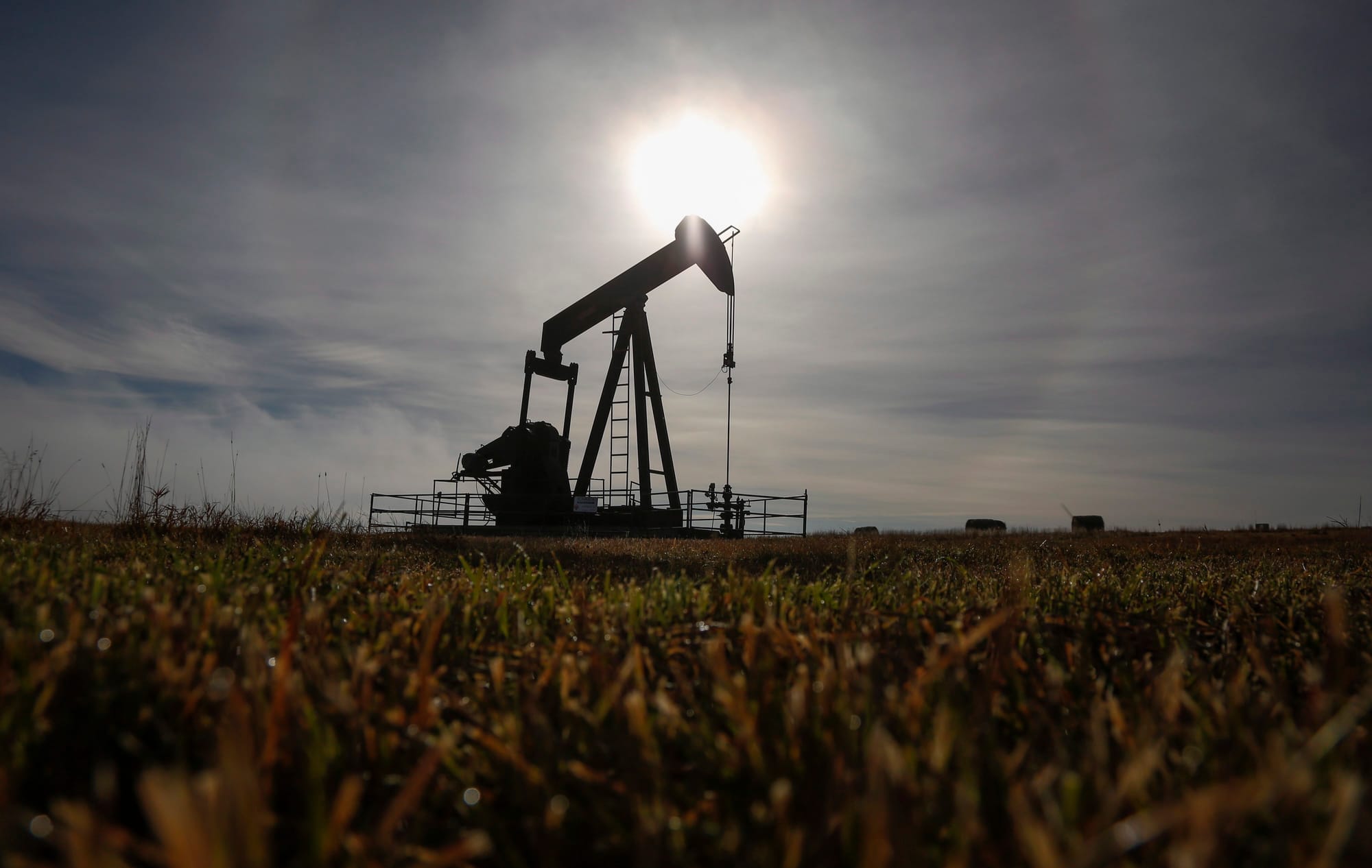 A pumpjack pictured in a yellow and green field against the backdrop of a cloudy sky. 