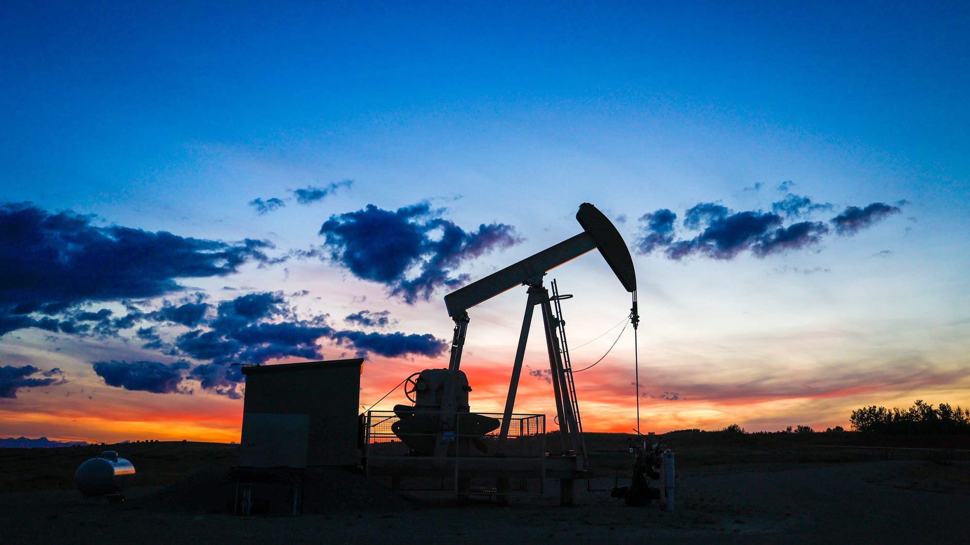 A pumpjack is seen drawing oil from a well head at sunset