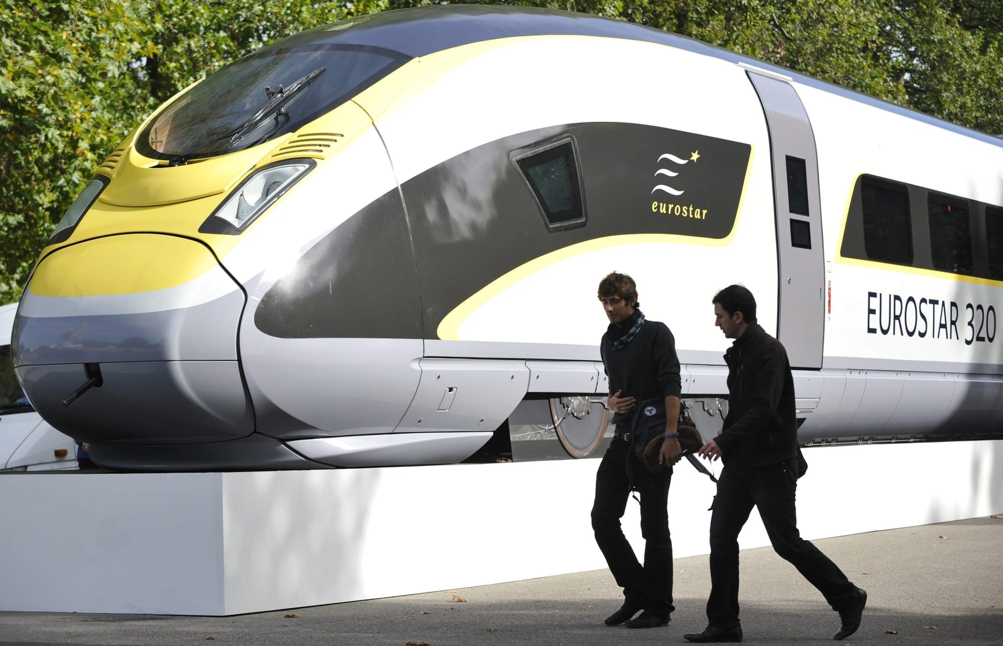 Two people are seen walking in front of a model European high-speed rail car