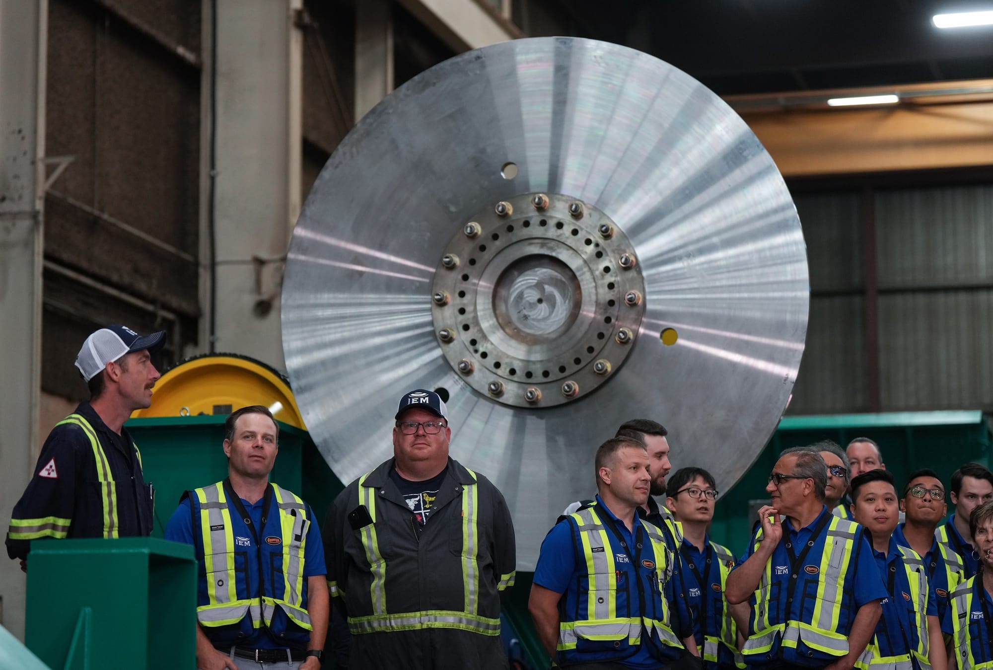 Workers in reflective, high-vis vests stand in front of a large piece of heavy machinery. 