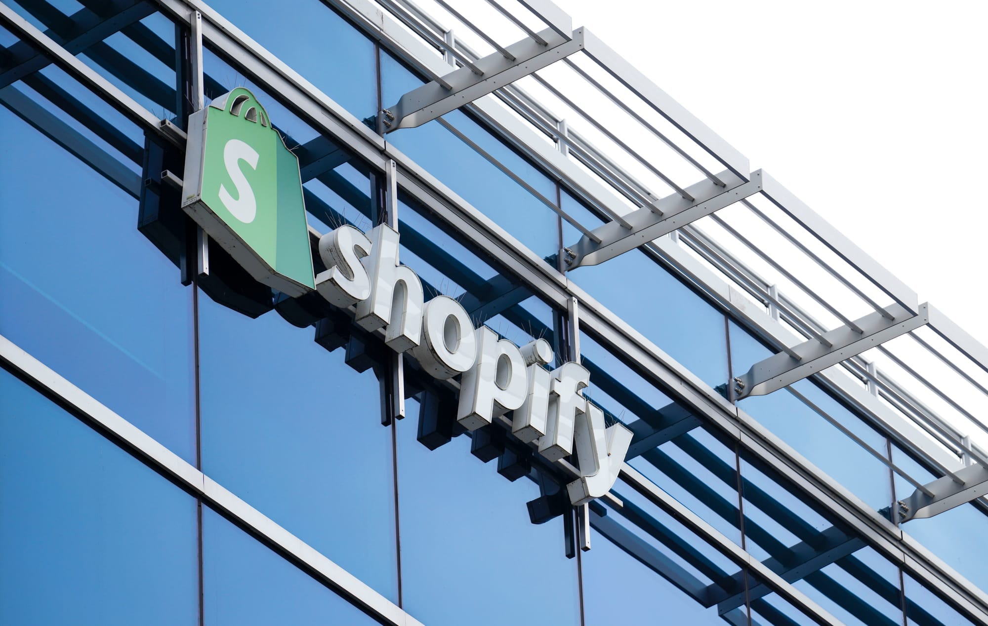 Signage featuring the Shopify logo is photographed on the outside of a glass office building 