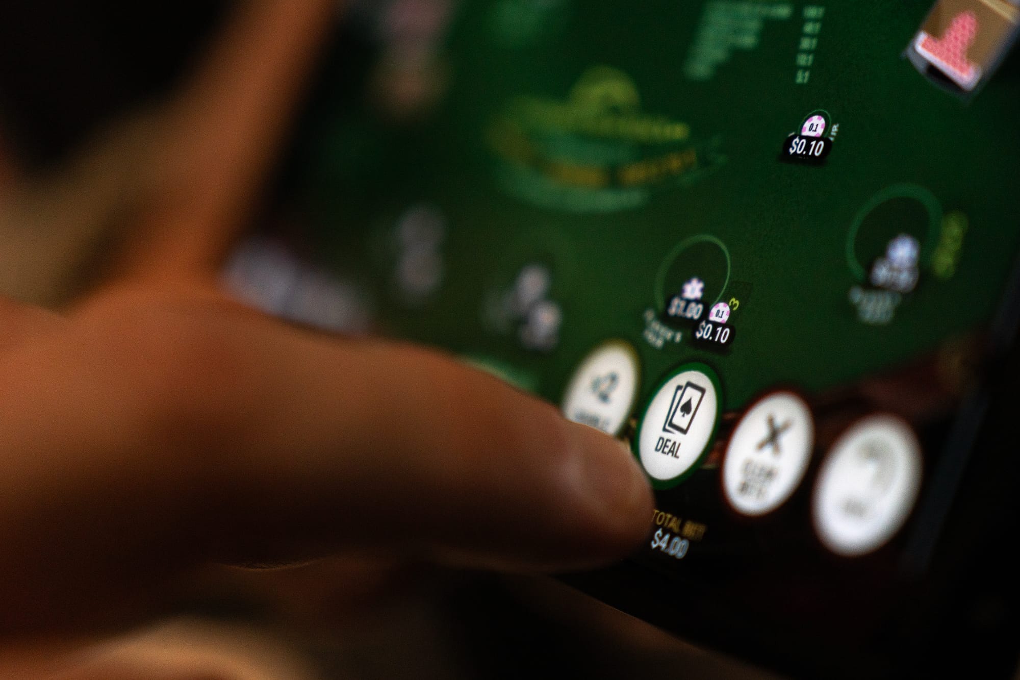 A hand presses a button on a touchscreen displaying an icon of a pair of playing cards. 