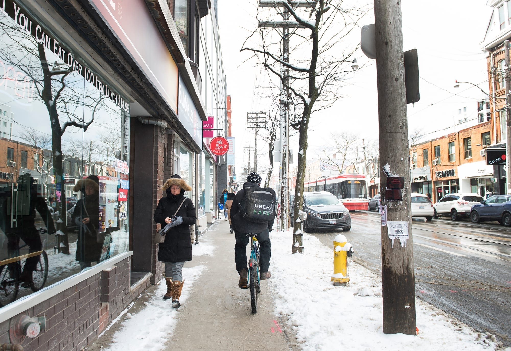 A person on rides a bike on a snowy sidewalk while wear a backpack that says "Uber Eats" 