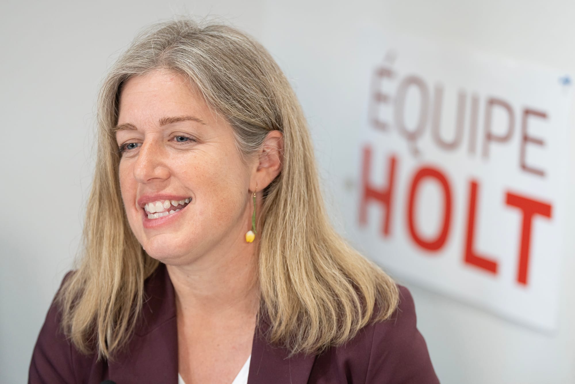 New Brunswick PremSusan Holt wears a maroon blazer in front of a sign that says "Equipe Holt"