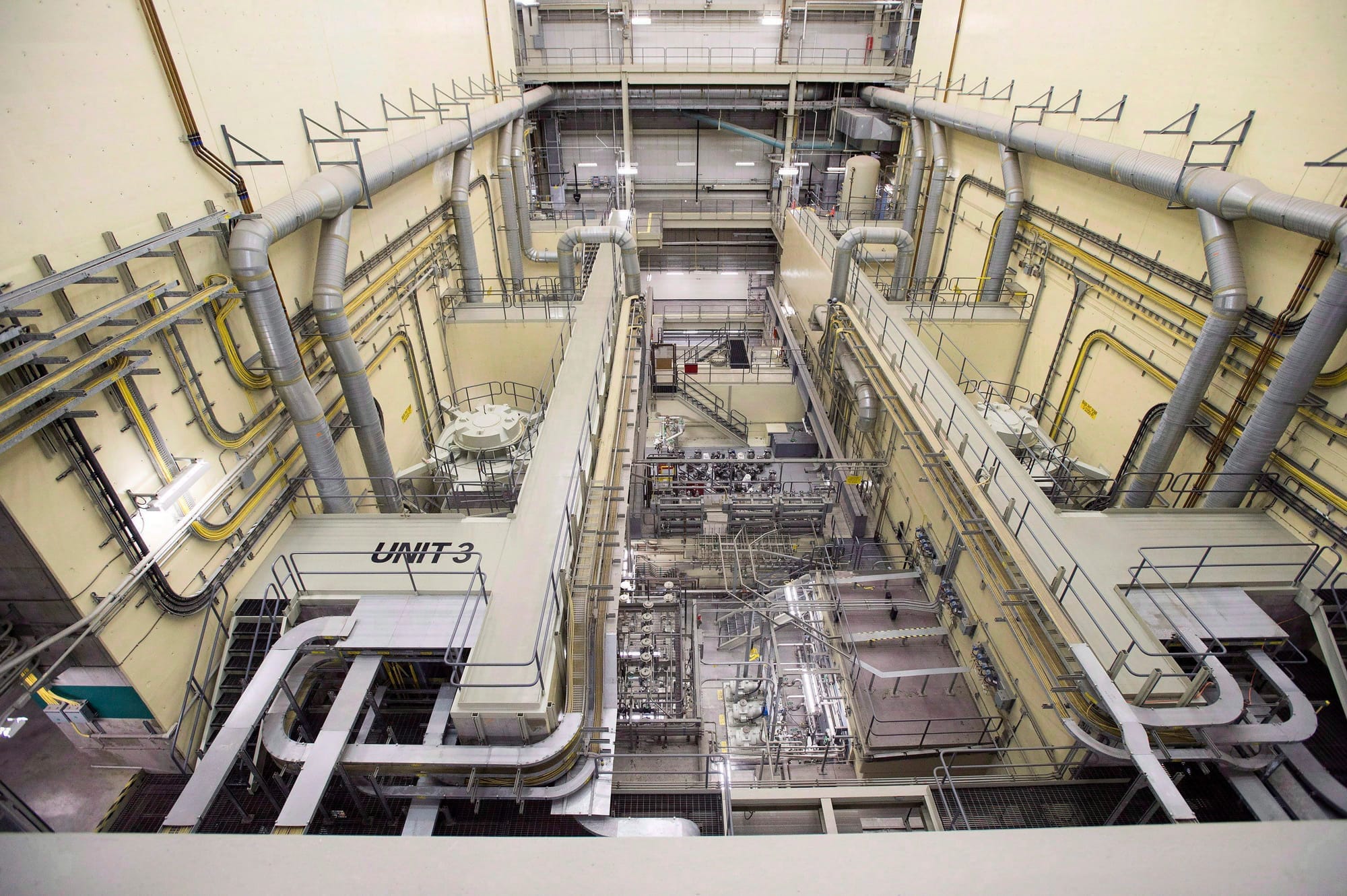 The inside of an industrial facility with metal pipes and concrete floors is seen from above.