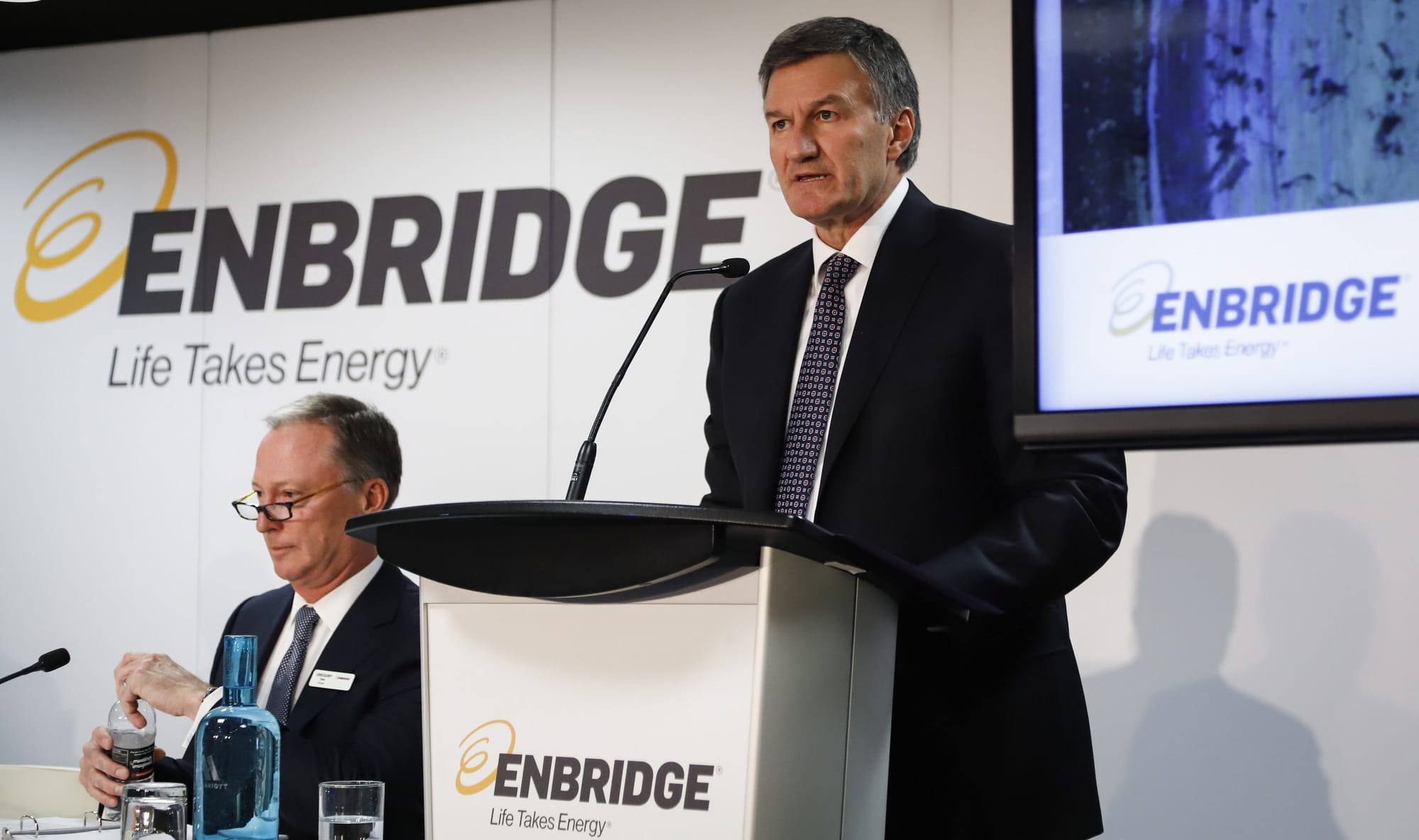 A man in a suit stands behind a podium with the Enbridge logo