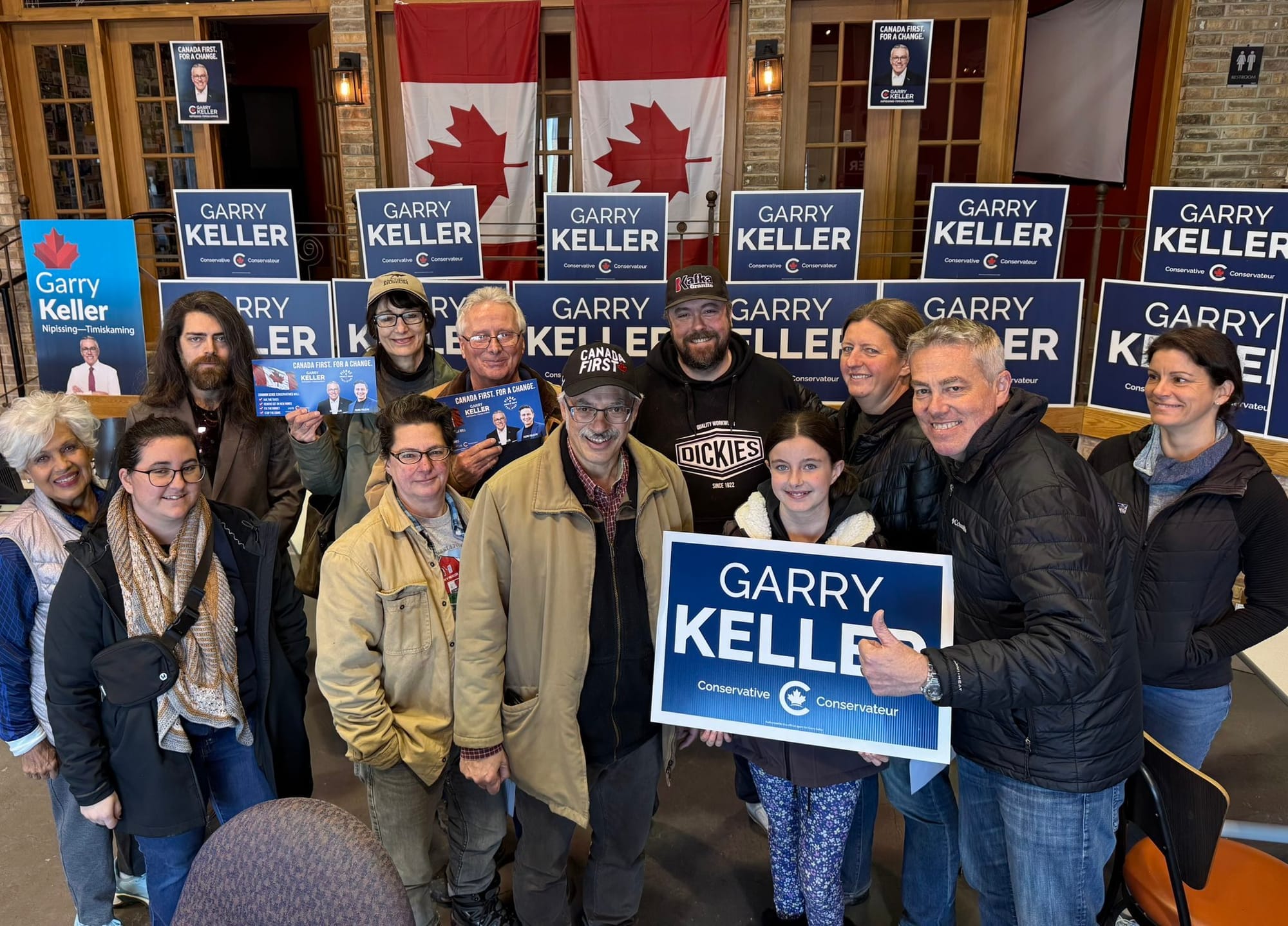 Supporters stan in front of blue signs that say "GARRY KELLER" in white lettering