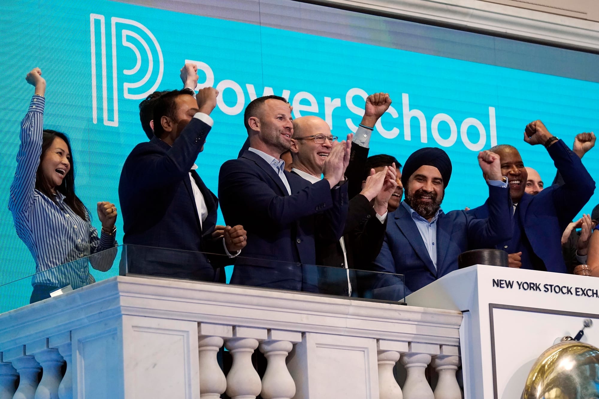 Executives cheer in front of a backdrop featuring the logo for software company PowerSchool