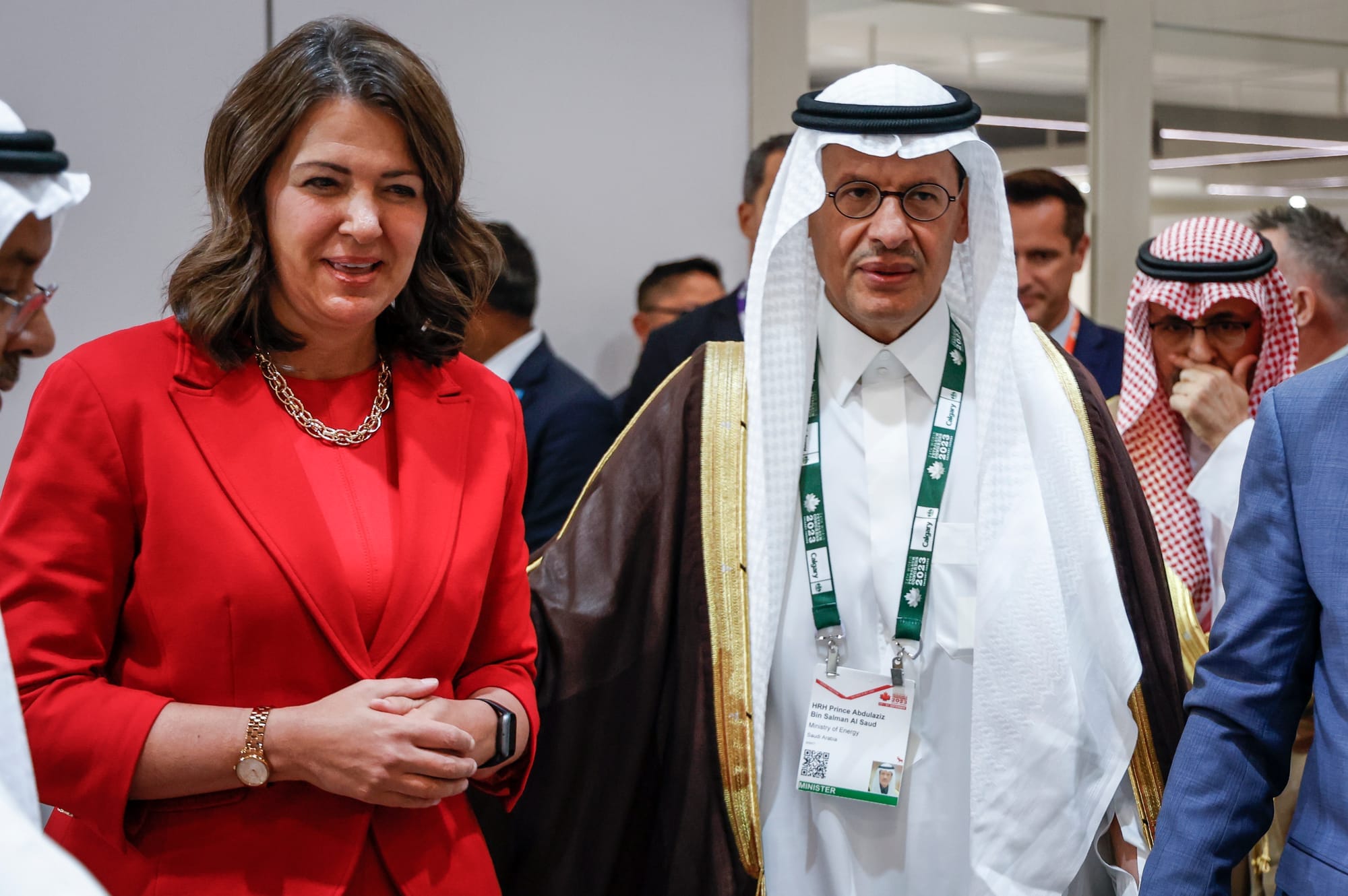 Danielle Smith wears a red suit next to a the Saudi Energy Minister, wearing a white Ghutra at an event