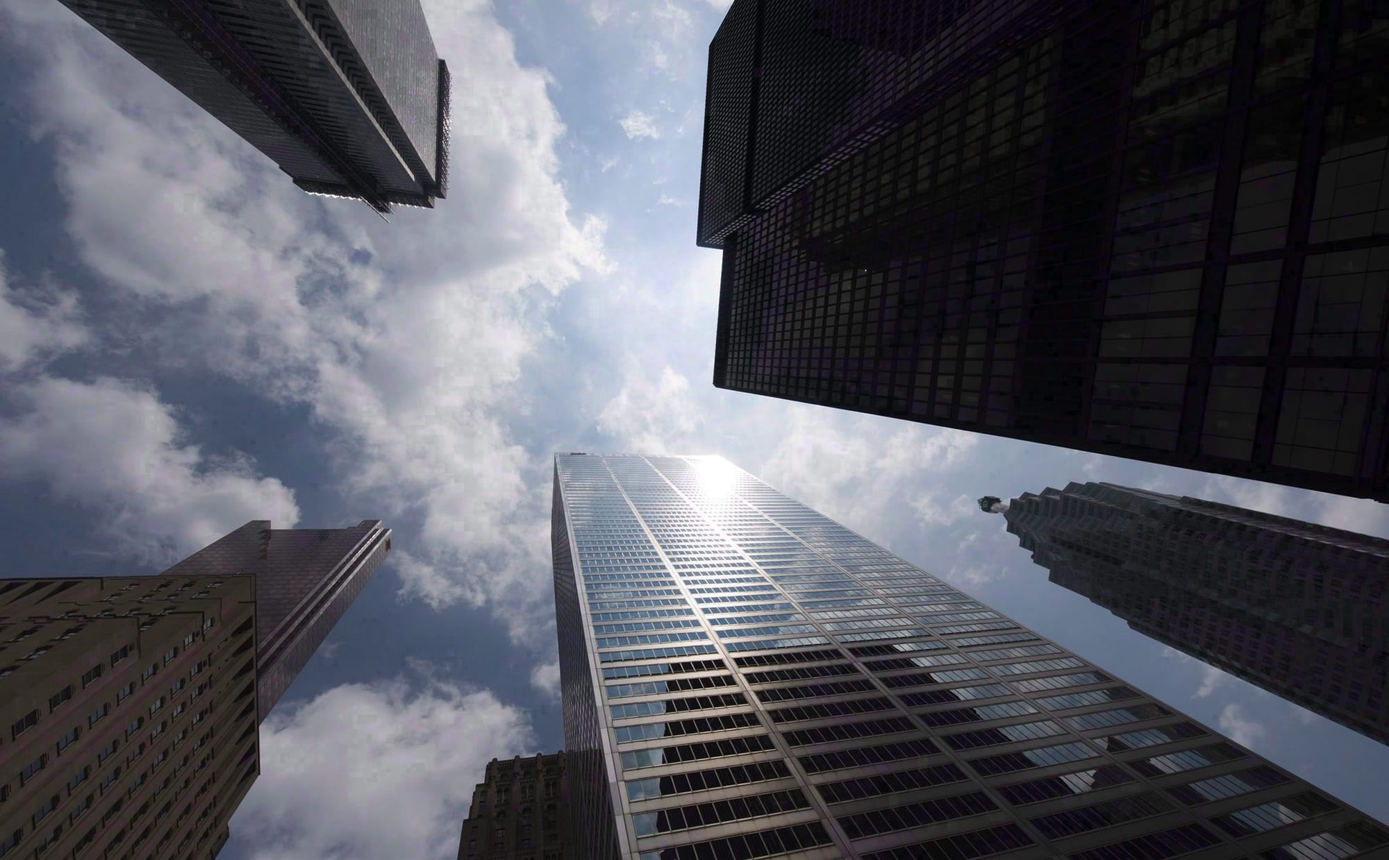 An upward shot depicting the tops of several skyscrapers against a bright blue sky. 