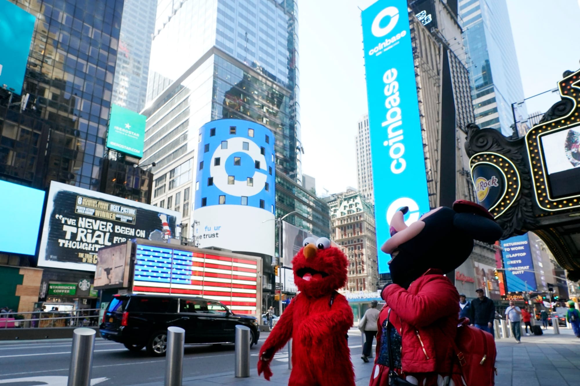 Costumed characters in New York's Times Square walk in front of a billboard for Coinbase