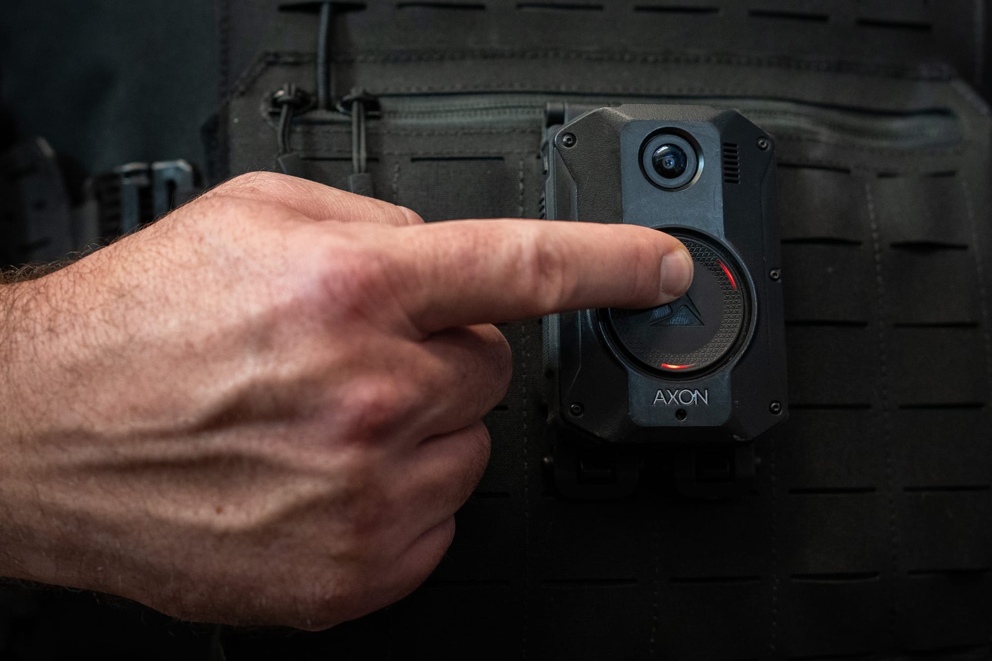 A hand presses on a body-worn camera attached to a police vest