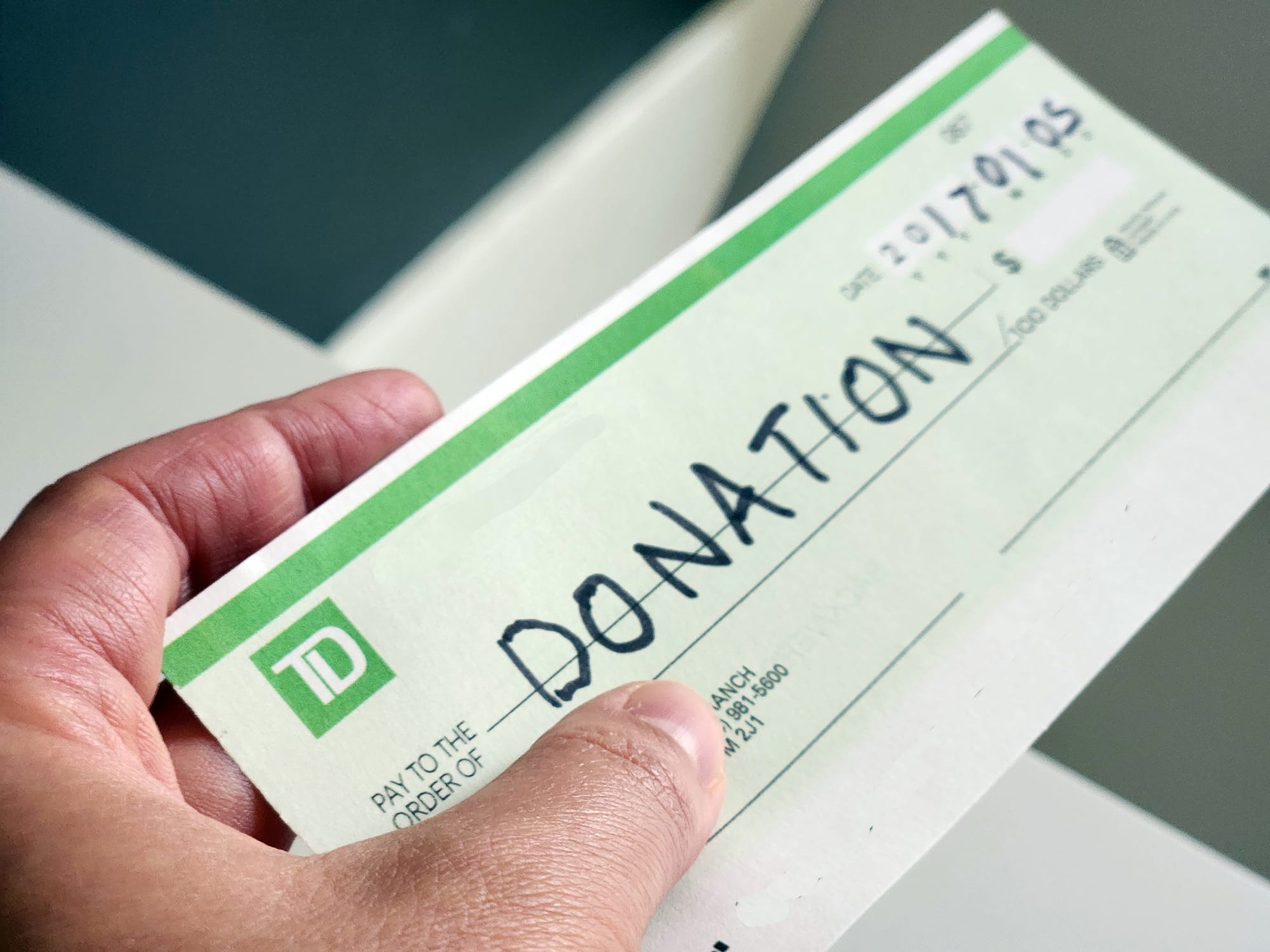 A hand holds a cheque made out to 'DONATION'.