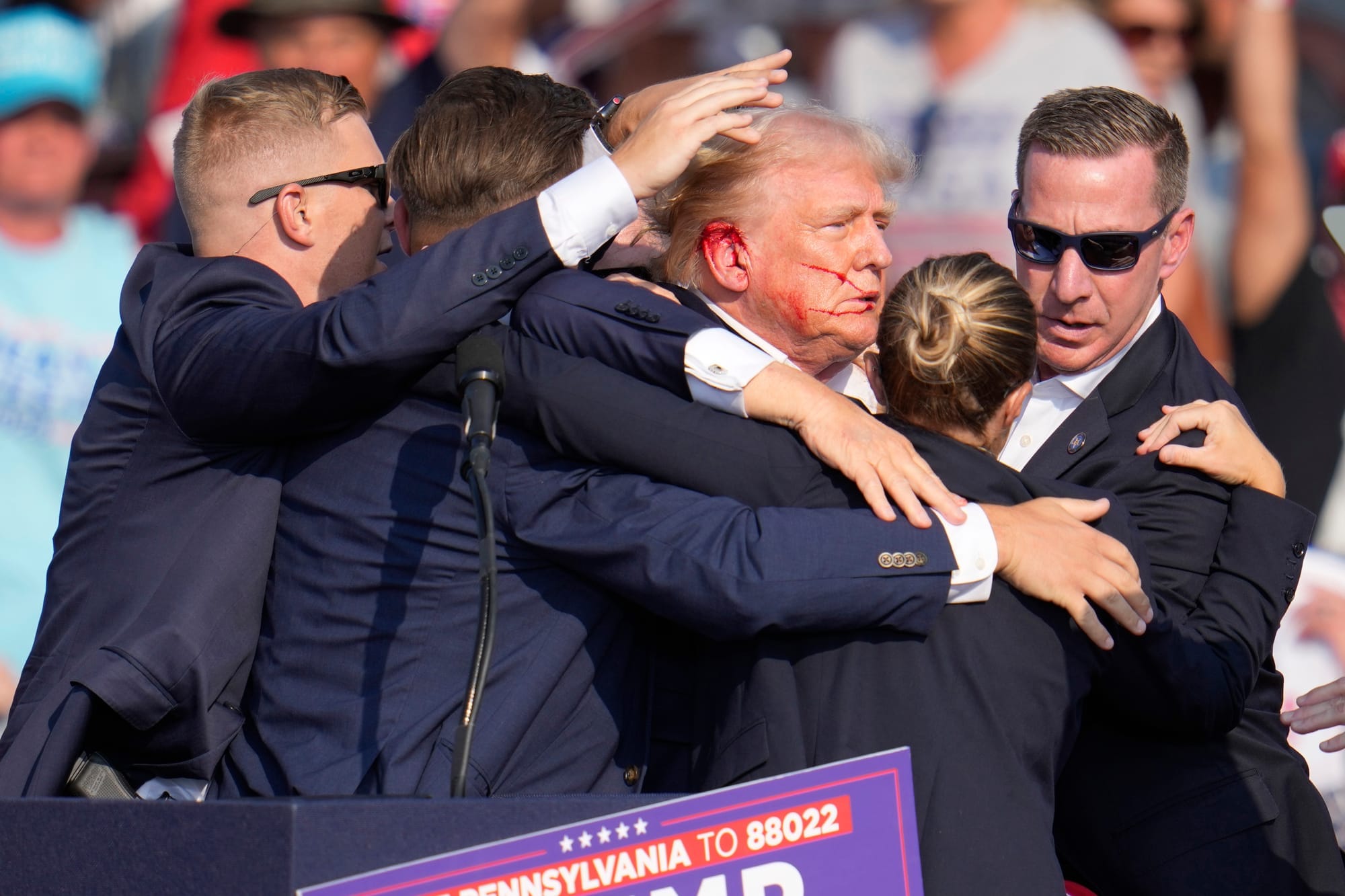 Donald Trump, with blood on his face, is swarmed by secret service agents at a rally after a gunman shot at him.