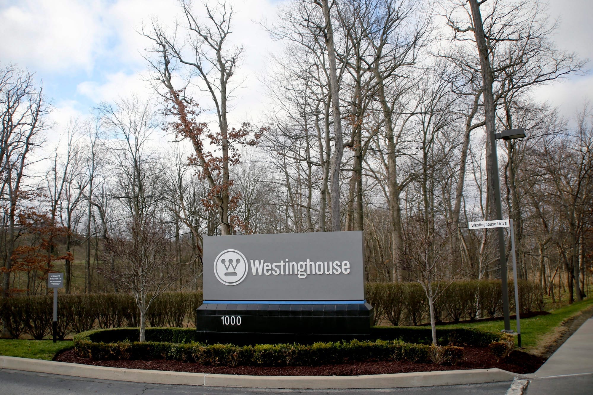 A grey sign that reads "Westinghouse" in white writing is seen outside in, front of trees with no leaves