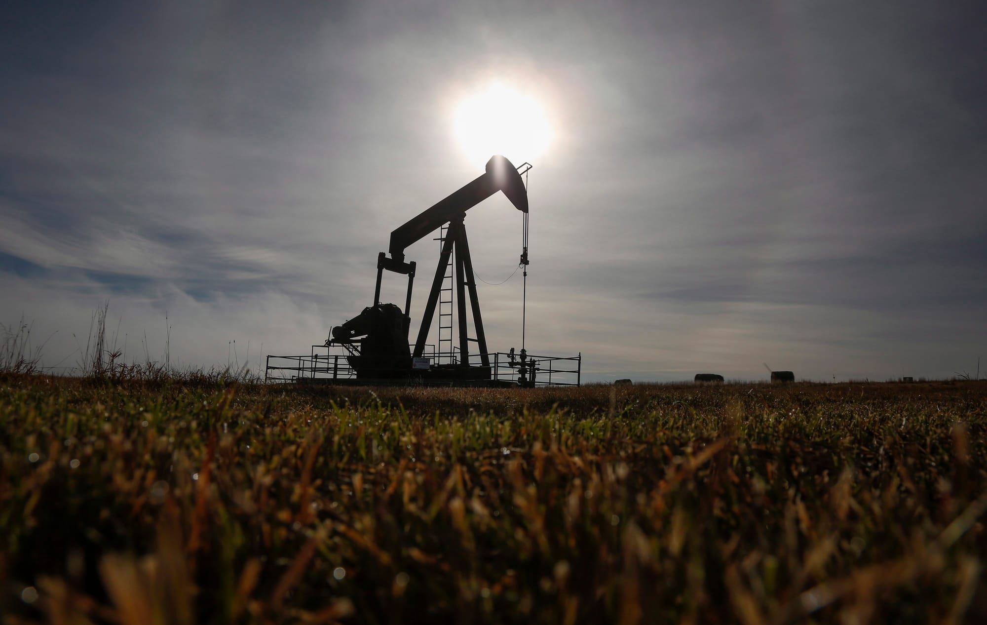 A pumpjack works at a well head on an oil and gas installation near Cremona, Alta., with a farm field in the foreground.