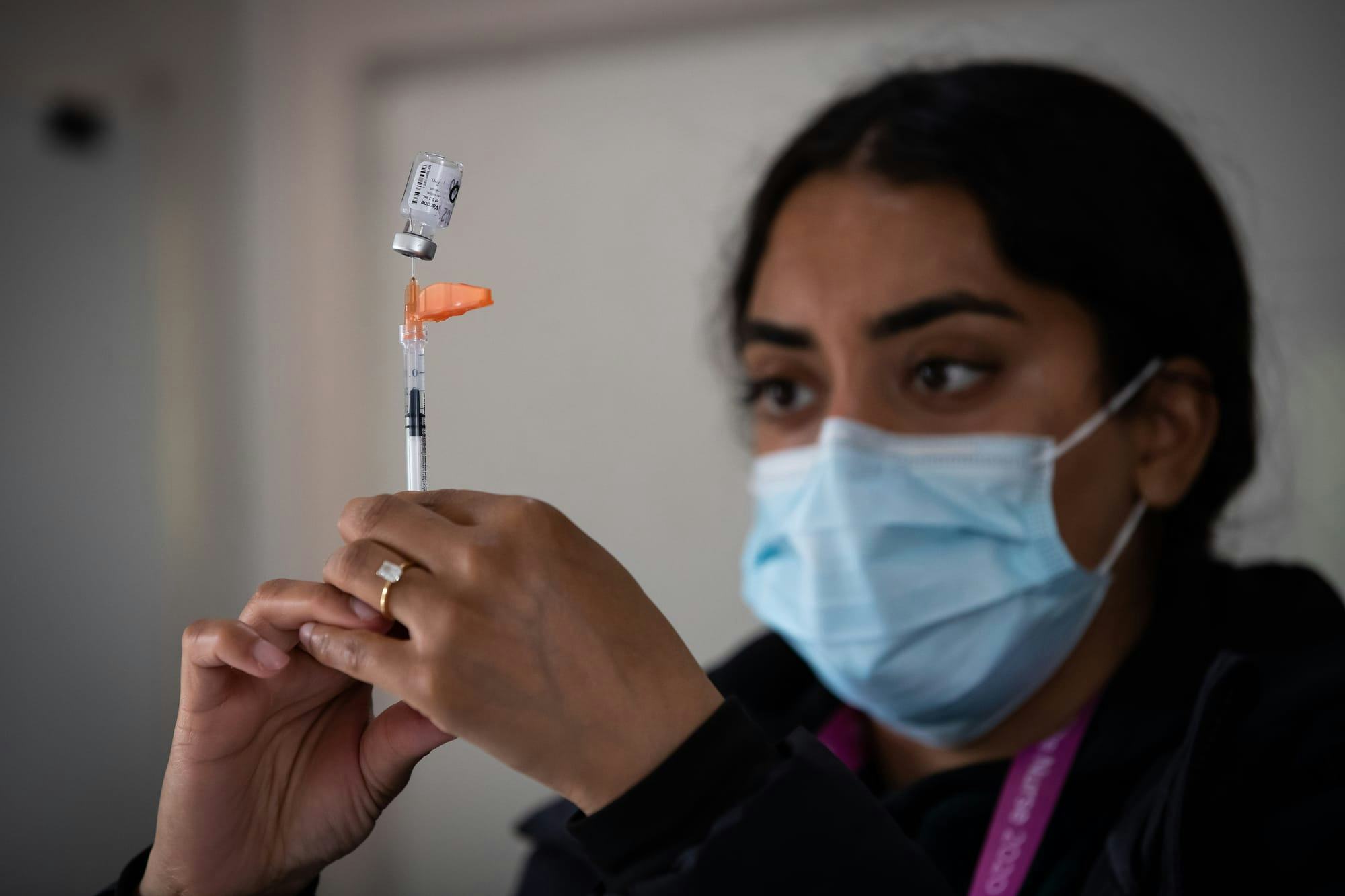 A nurse, wearing a mask, pulls a dose of a COVID-19 vaccine into a syringe.