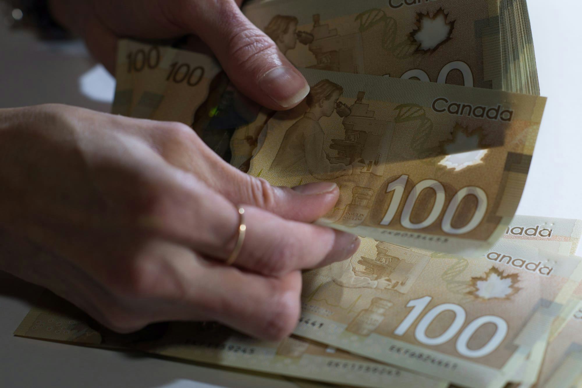 Two hands are shown in closeup, counting $100 Canadian bills.