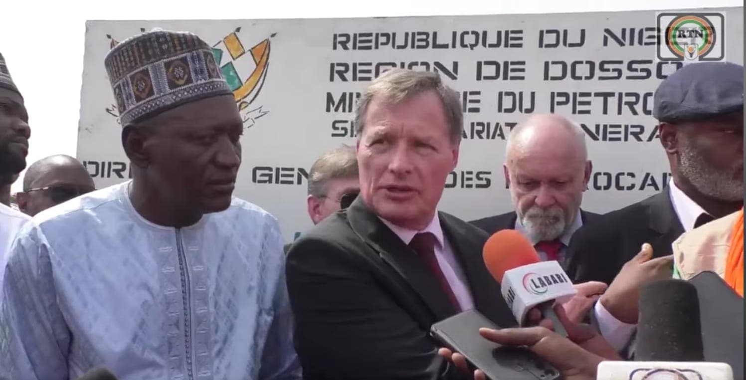 A man in a white embroidered shirt stands next to a man in a suit and tie at a press conference.