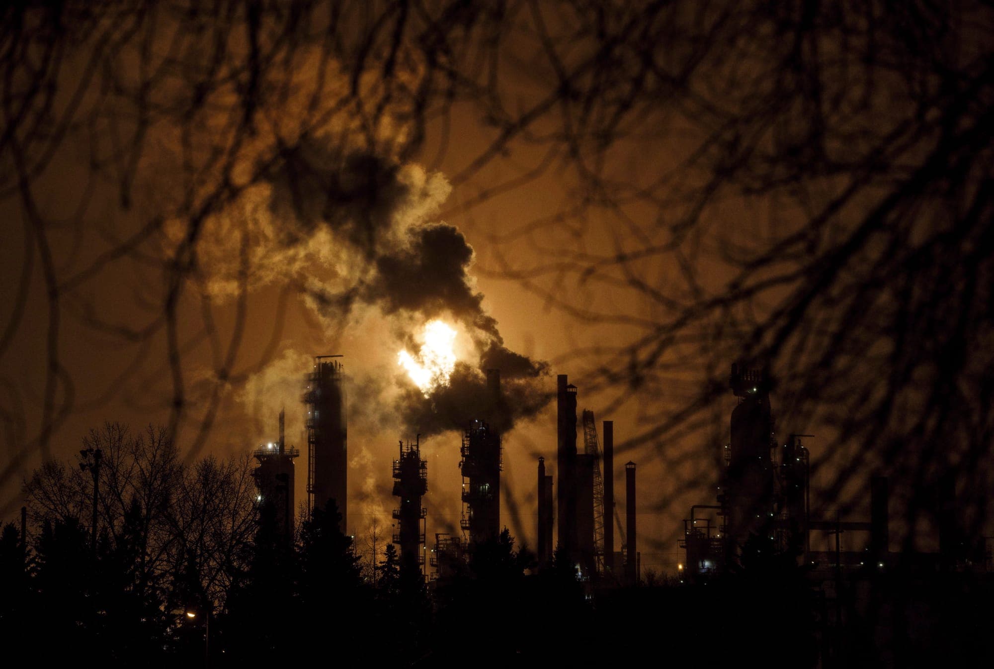 Flames and smoke rise from flare stacks against a brown sky.